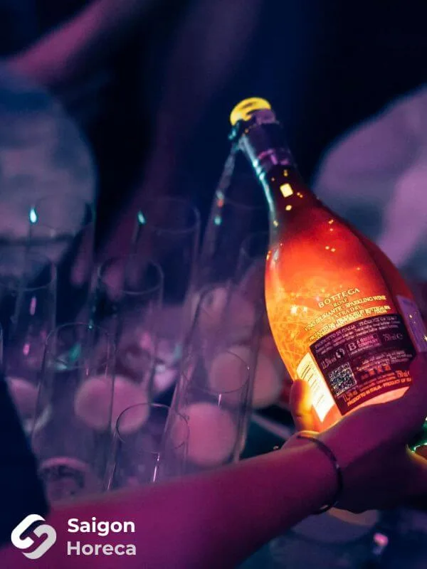 Chai vang nổ Bottega phát sáng cầm trên tay bên dàn ly cao tại Bling Bling Club