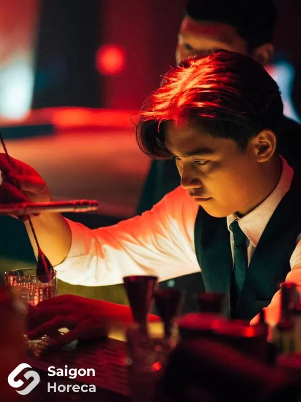 Bartender mặc sơ mi vest tập trung pha chế cocktail tại quầy bar Bling Bling Club