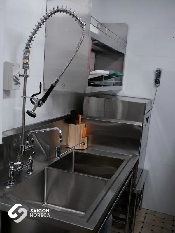 Chậu rửa inox hai ngăn với vòi xịt tiền rửa lò xo và giá dao thớt gỗ tại khu sơ chế bếp Nam An