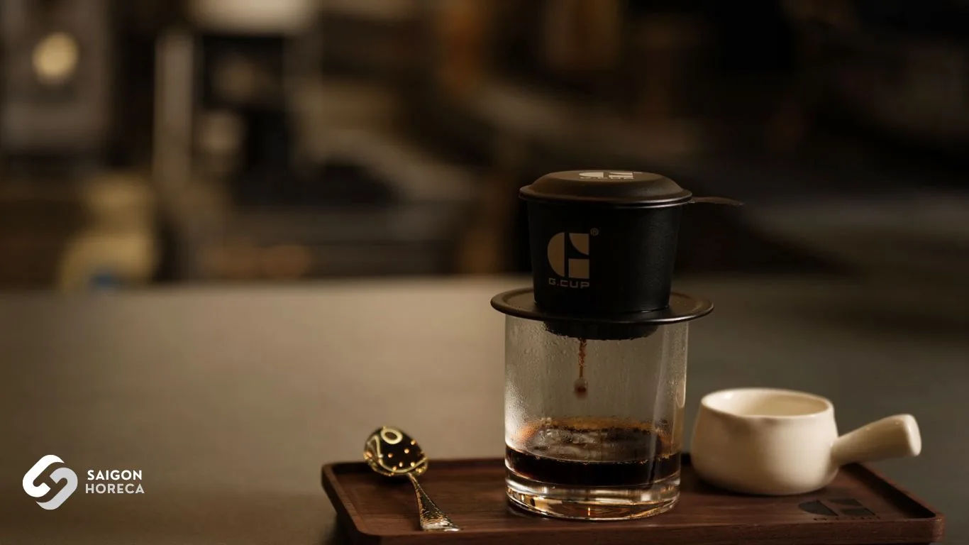 Phin cà phê nhôm đen logo G.Cup nhỏ giọt xuống ly thủy tinh trên khay gỗ