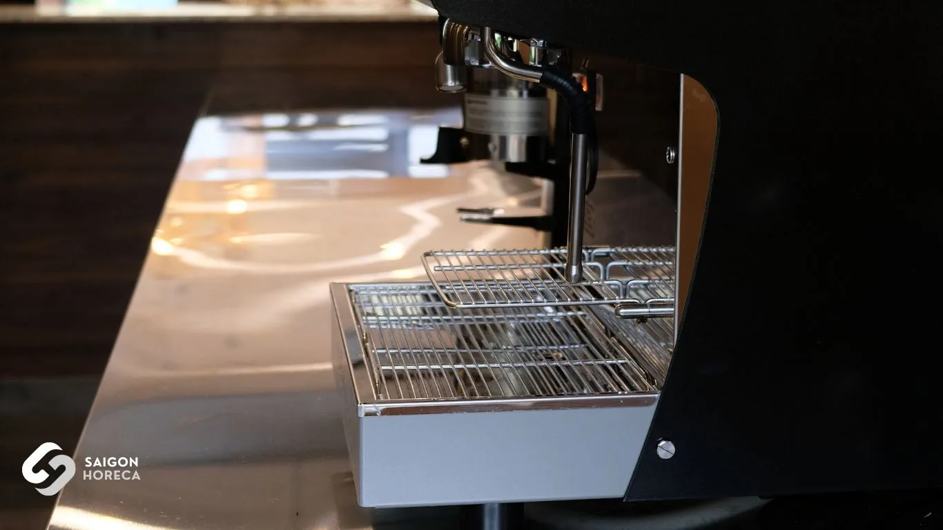 Cận cảnh khay hứng lưới inox của máy pha espresso trên mặt bàn inox – đường nét gia công tinh xảo