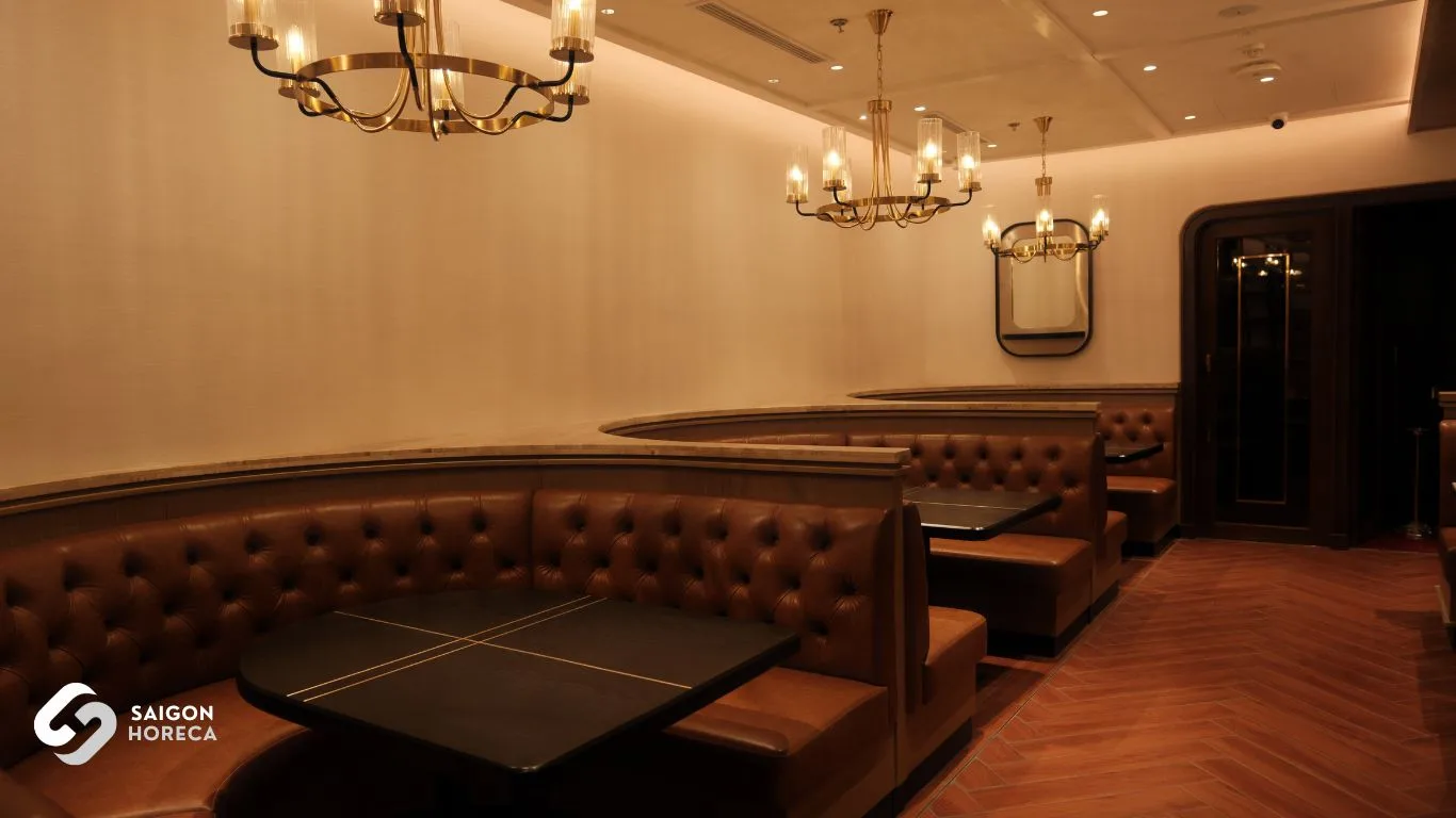 Dãy ghế sofa da nâu ấm cúng dưới ánh đèn chùm cổ điển tại The Royal